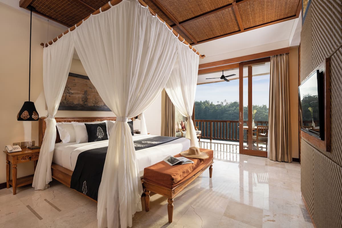 Un dormitorio con cama con dosel, un banco de madera, una mesita de noche y un ventanal con vistas al exterior.