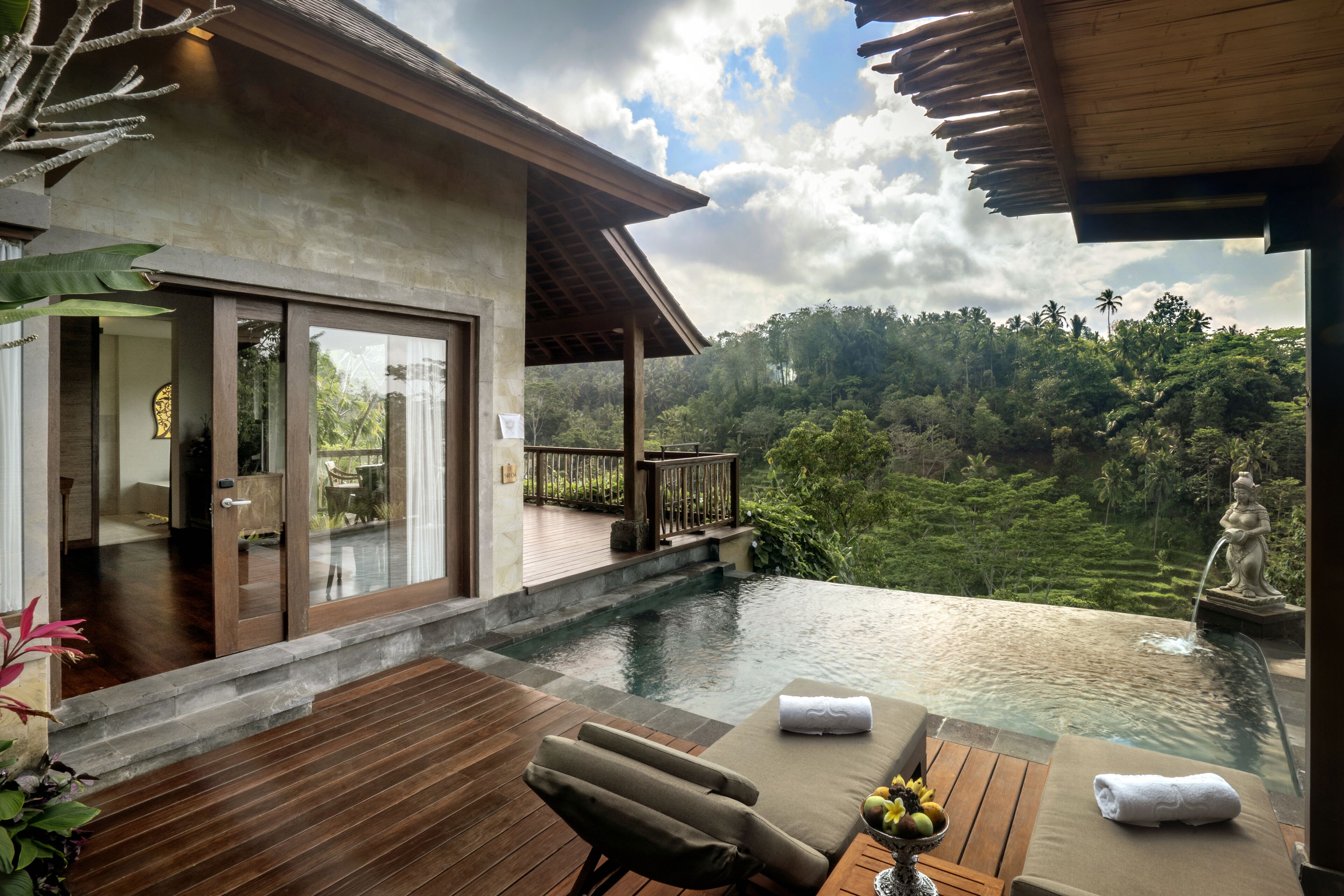 Une villa moderne dotée d’une piscine à débordement privée, d’une terrasse en bois et d’une végétation luxuriante en arrière-plan.