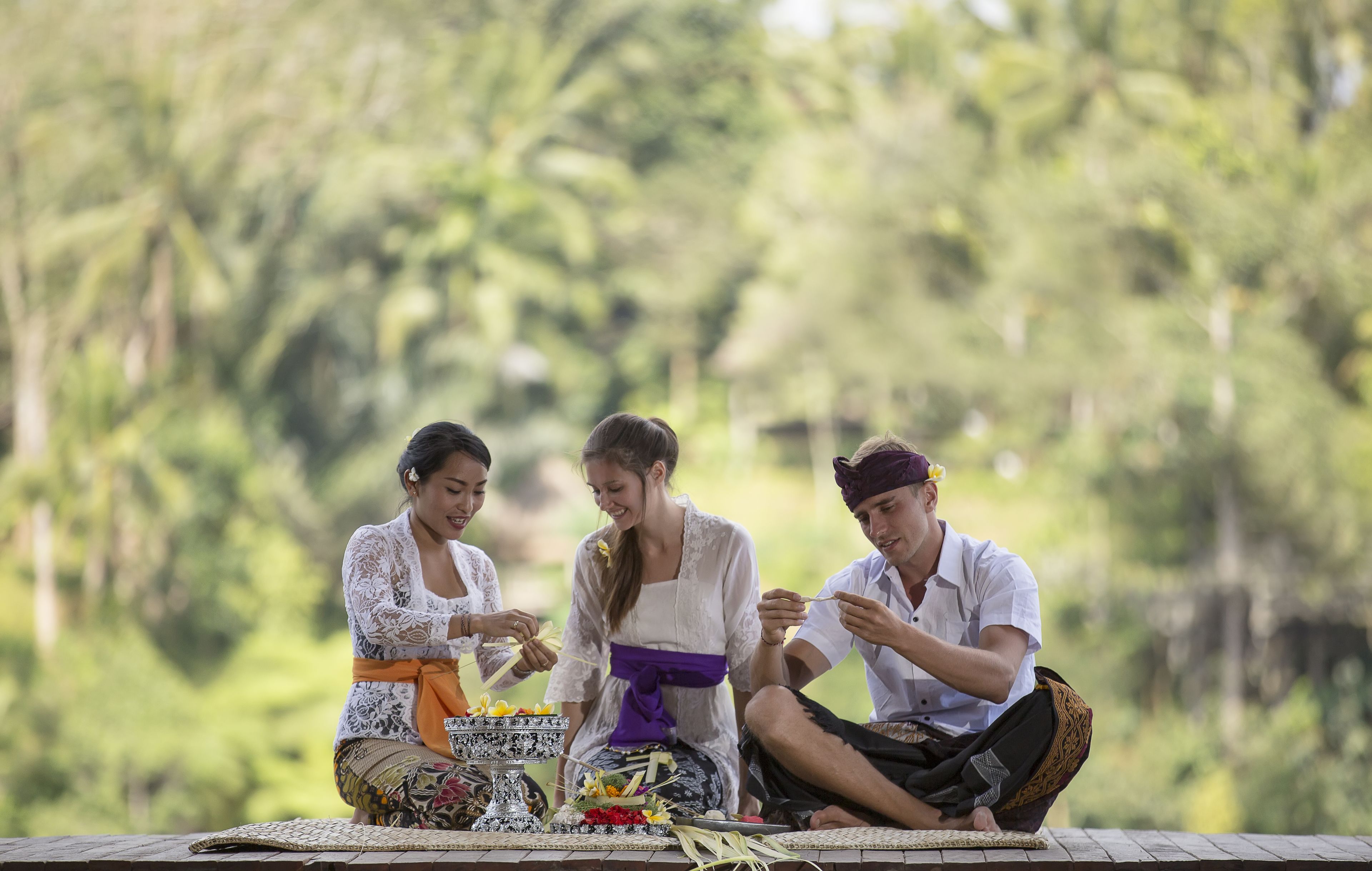 Three people sitting on a wooden platform outdoors with a lush green background.