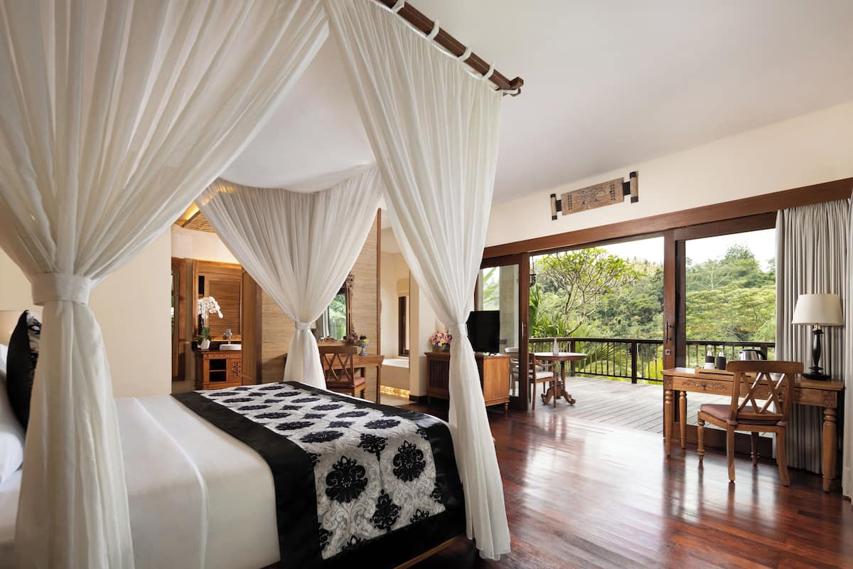 Un dormitorio con cama con dosel, un escritorio y una silla, y un balcón con vistas al exterior.
