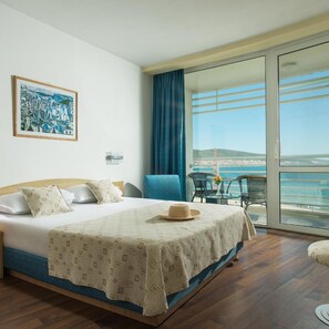 A hotel room with a bed, a painting, a balcony with a table and chairs, and a view of the sea. - Effect Grand Victoria Hotel (Sunny Beach)