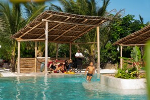 Un área de piscina con un pabellón de madera, palmeras y una piscina azul cristalina.