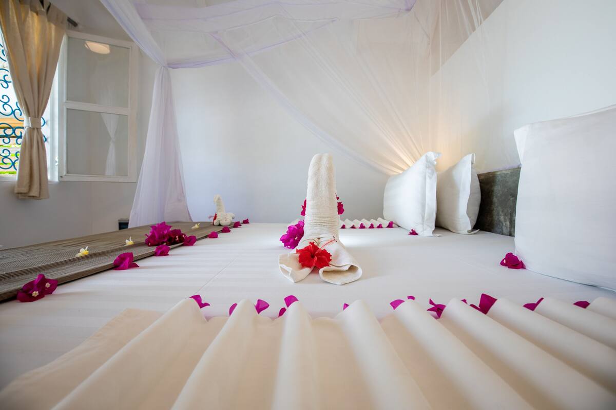 Una habitación de hotel con una cama, cortinas blancas, un ventanal y un espejo.