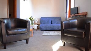 Un salon avec deux fauteuils en cuir, un canapé bleu, une petite table sur laquelle est posé un vase, et un téléviseur sur un meuble en bois.