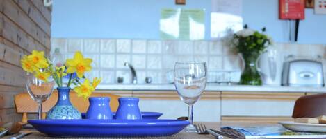 Una mesa de comedor con un plato azul, dos jarrones con flores amarillas y una copa de vino.