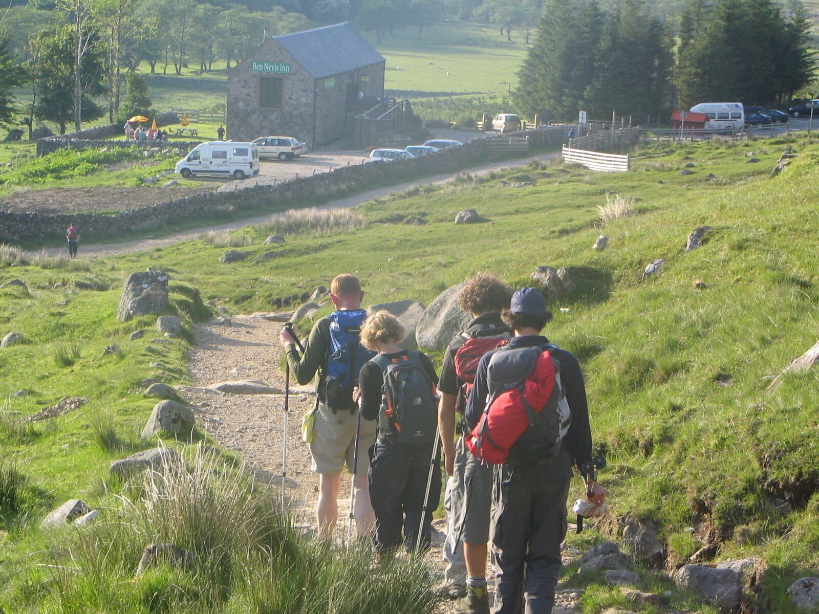 Ein Steinhaus mit der Aufschrift "Ben Nevis Inn", zu dem ein Feldweg führt, umgeben von Grünpflanzen und parkenden Fahrzeugen.