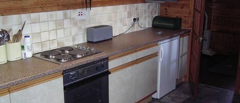 A compact kitchen with a stove, microwave, toaster, and a small refrigerator.