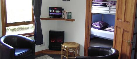A compact room with a television, a small table, two chairs, a bunk bed, and a fireplace.