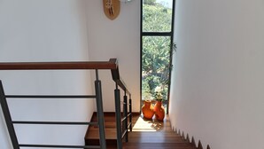 A wooden staircase with a metal handrail leading to a room with a large window and two terracotta pots on the floor. - The Designhouse by Our Madeira (Calheta)