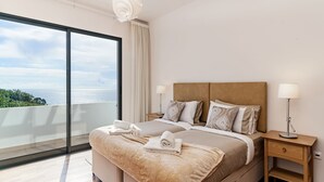 A modern bedroom with a large bed, two bedside tables, and a view of the ocean. - The Designhouse by Our Madeira (Calheta)