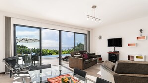 A modern living room with a glass table, a sofa, and a TV. - The Designhouse by Our Madeira (Calheta)