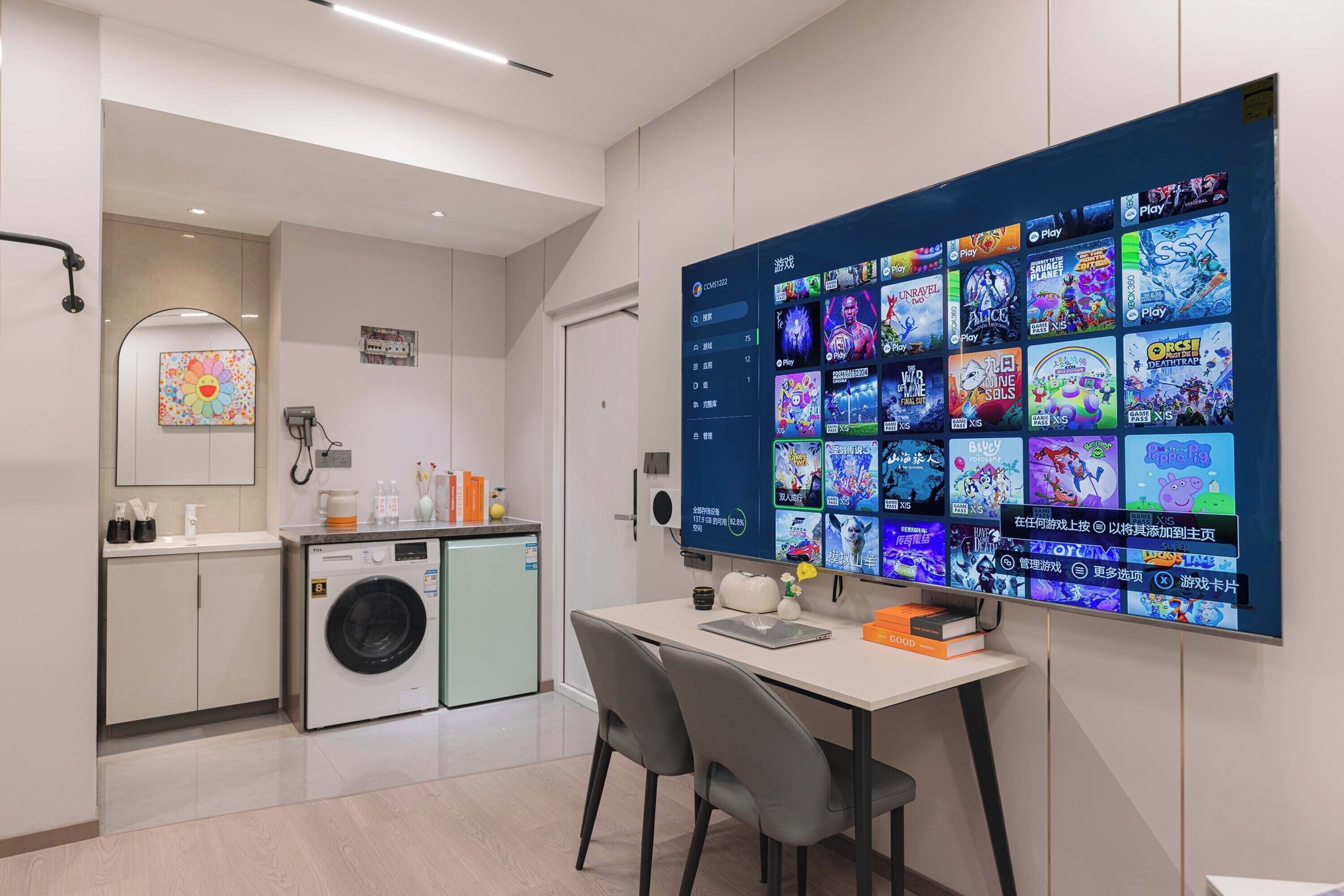 A modern hotel room with a large digital display wall, a compact kitchenette, and a seating area with a table and chairs.