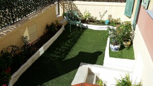 A small, enclosed garden area with artificial grass, potted plants, and a green chair. - Hotel Marcellin (Beaulieu-sur-Mer)