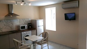 A compact kitchen with a microwave, coffee maker, and a refrigerator. There's a washing machine, a dining table with chairs, and a TV mounted on the wall. - Hotel Marcellin (Beaulieu-sur-Mer)