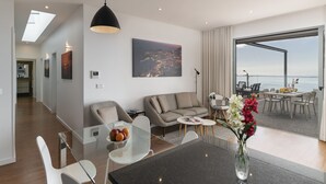 Een moderne woonkamer met een glazen eettafel, een bank en een groot raam met uitzicht op de stad.