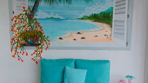 Una stanza con un divano color petrolio, un tavolino bianco e un quadro raffigurante una spiaggia.