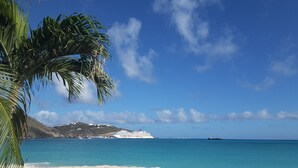 Una spiaggia con sabbia bianca, acqua cristallina turchese e una nave da crociera all'orizzonte.