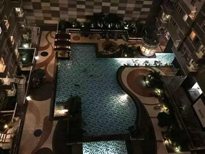 An aerial view of a hotel courtyard with a central pool, surrounded by lounge areas and a checkered floor pattern.