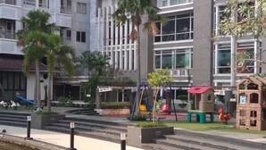 A playground with slides and swings, surrounded by palm trees and a building with large windows. - Apartment Sudirman Park 2 Bedrooms & 2 Bathrooms Jakarta (Jakarta)
