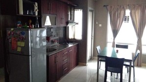 A kitchen with dark wooden cabinets, a stainless steel refrigerator, and a dining area with a glass table and chairs. - Apartment Sudirman Park 2 Bedrooms & 2 Bathrooms Jakarta (Jakarta)