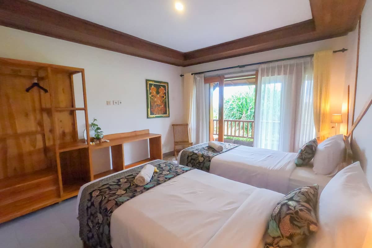 Ein Hotelzimmer mit zwei Betten, einem Holzschrank, einem Schreibtisch und einem Balkon mit Vorhängen.
