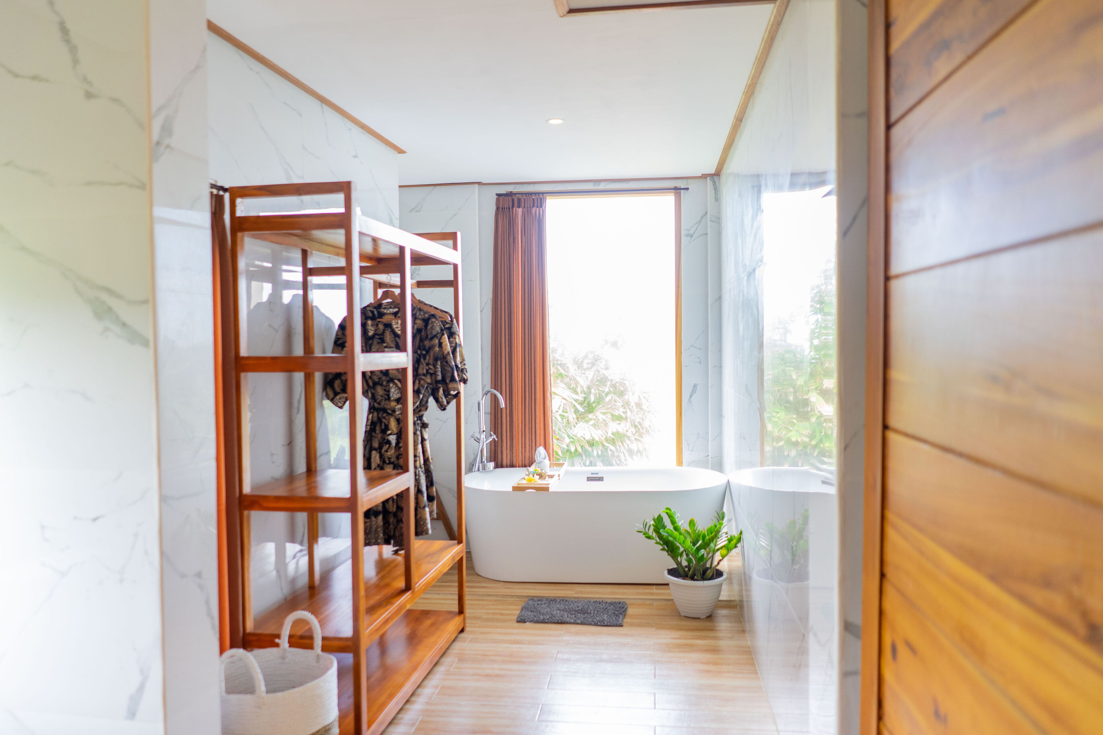 A modern bathroom with a wooden vanity, a bathtub, and a potted plant.