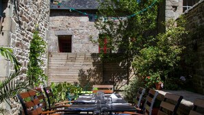 Un área de comedor al aire libre con paredes de piedra, bancos y mesas de madera.