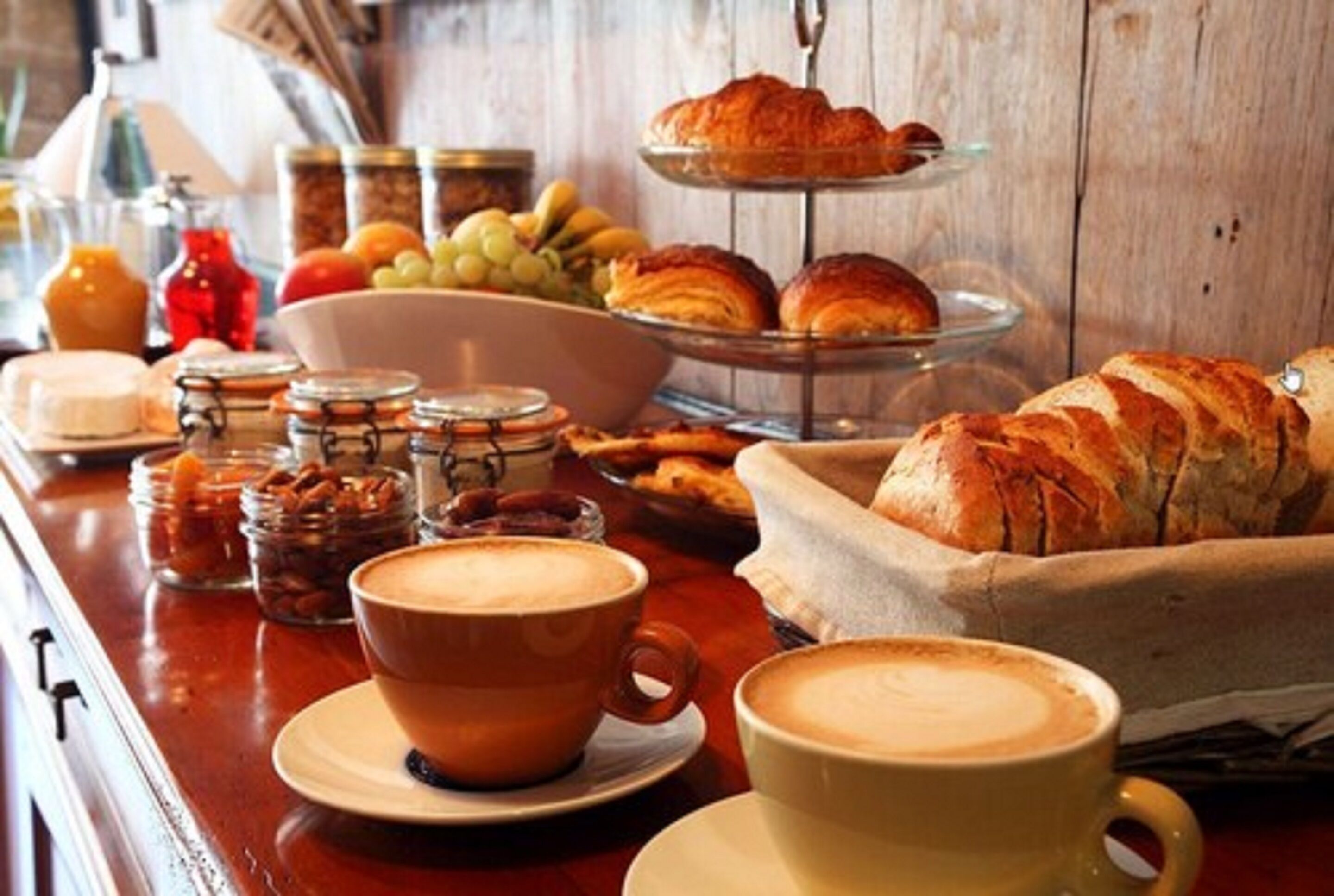 Ein Frühstückstisch mit Croissants, Gebäck und Kaffeetassen aus Holz.