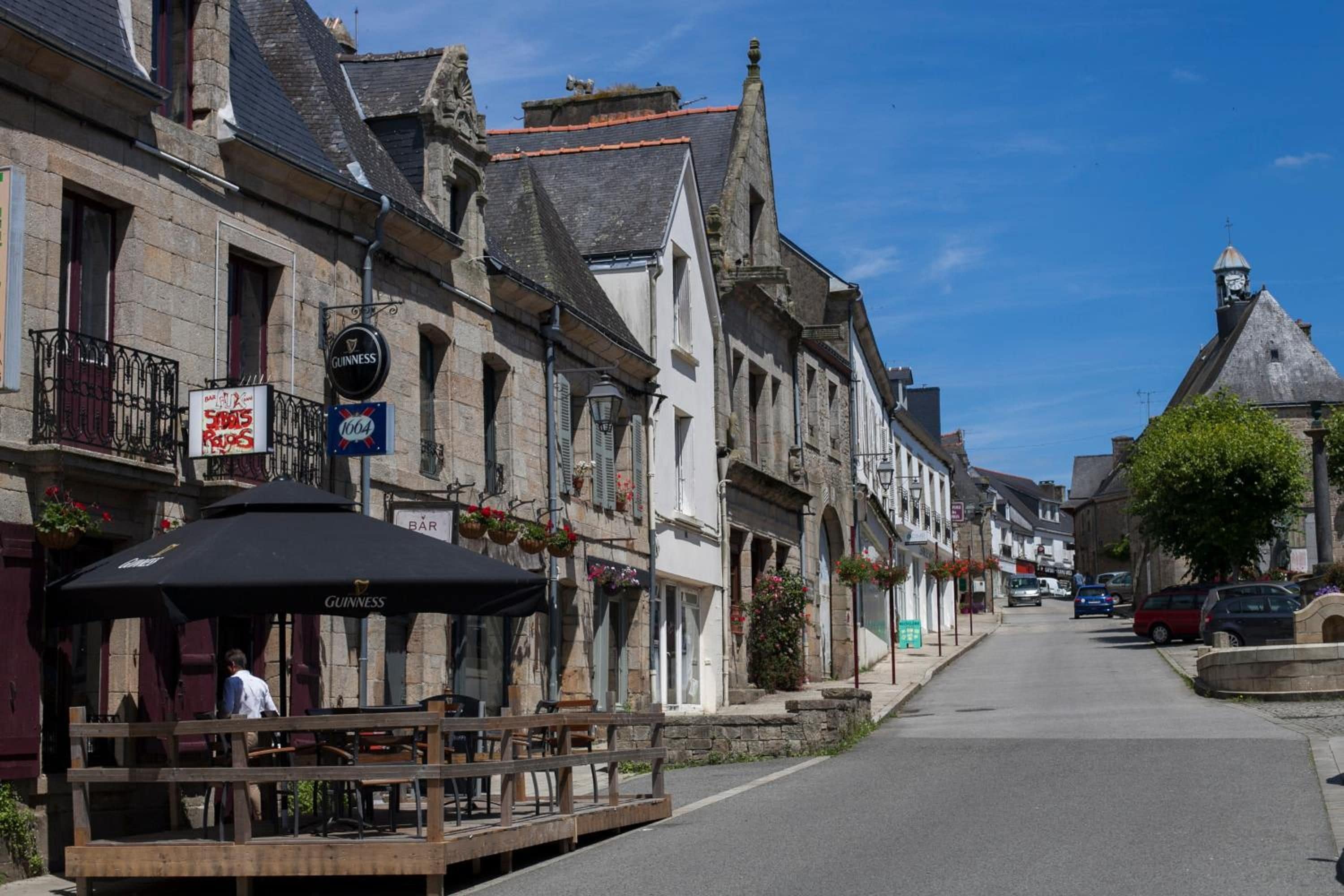 A street with traditional European architecture, including stone buildings with gabled roofs and a clear blue sky.