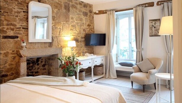Un dormitorio con pared de piedra, cama, televisor, silla y ventana con cortinas.