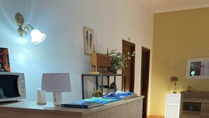 A reception area with a wooden reception desk, a wall-mounted lamp, a framed picture, and a small table with a vase. - Pension Porto Carral (Muros)