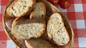 A basket of sliced bread, a glass of orange juice, a bottle of olive oil, and fresh tomatoes on a checkered tablecloth. - Pension Porto Carral (Muros)
