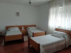 A room with two single beds, a bedside table with a lamp, a small framed picture on the wall, and a window with sheer curtains. - Pension Porto Carral (Muros)