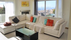 Una sala de estar moderna con un sofá modular, una mesa de centro de vidrio y vistas al mar a través de amplios ventanales.