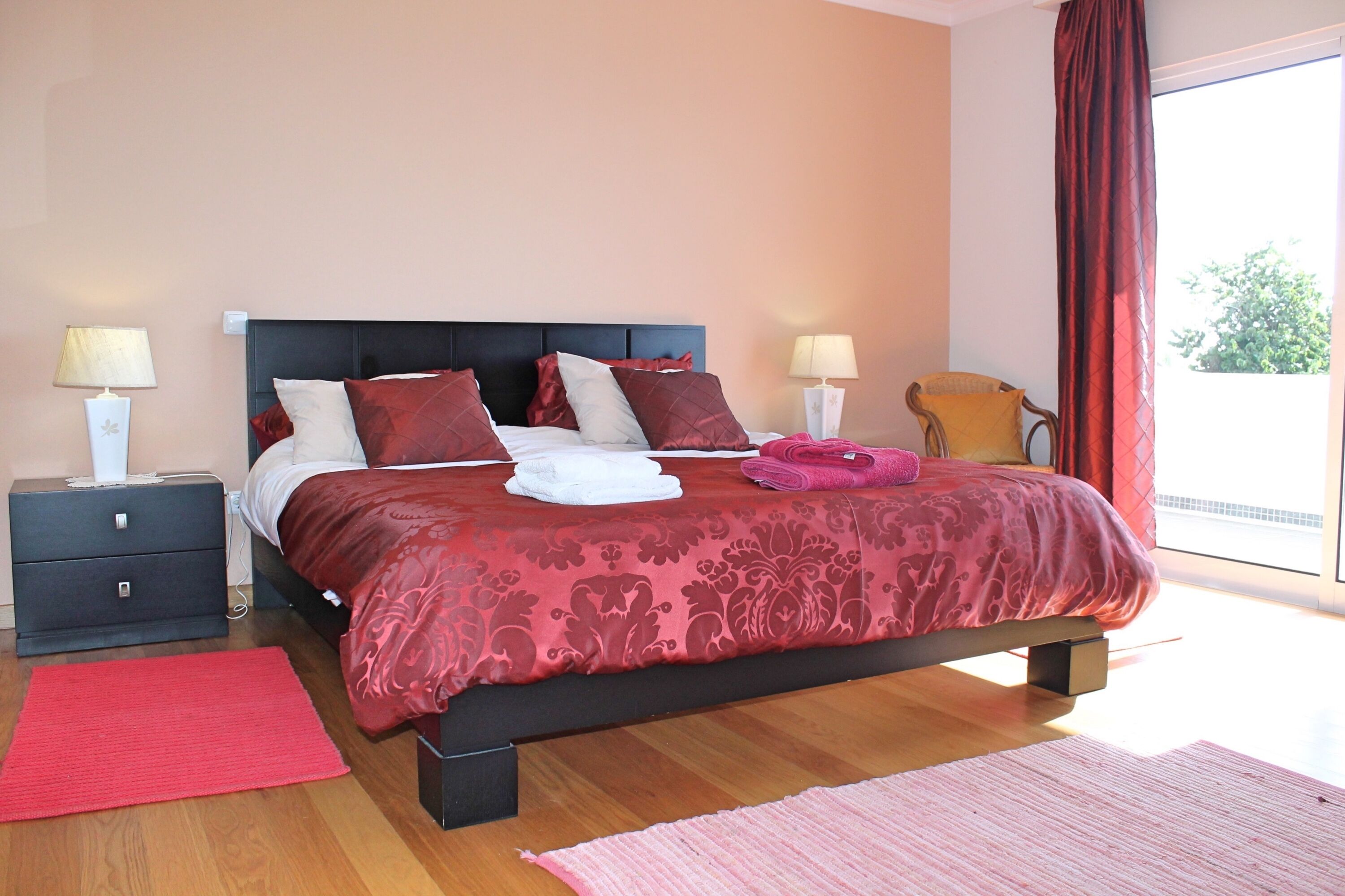 Een slaapkamer met een groot bed, twee nachtkastjes, een stoel en uitzicht op het omliggende landschap.