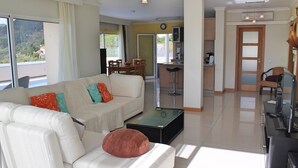 Amplia sala de estar con sofá, mesa de centro y mesa de comedor con sillas. Se observa una zona de cocina al fondo, con refrigerador y microondas.
