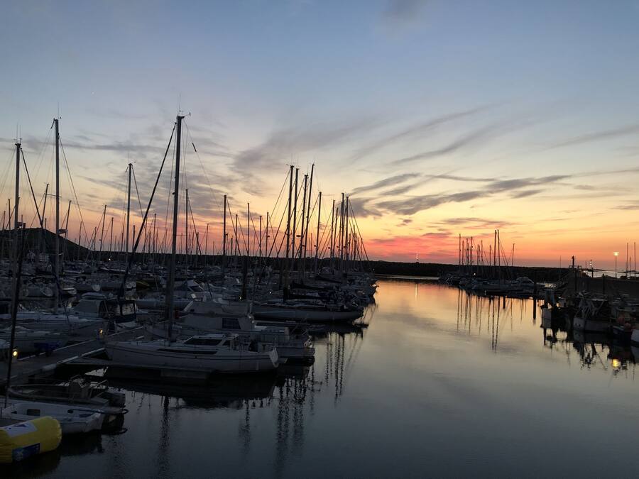 Ein Yachthafen mit zahlreichen Booten, die im ruhigen Wasser bei Sonnenuntergang liegen.
