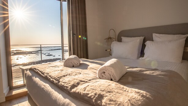 Habitación de hotel con una cama grande, vista a la playa y un balcón con cortinas.