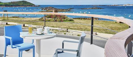 Een terras met tafel en stoelen met uitzicht op de kust, boten en rotsachtig terrein.