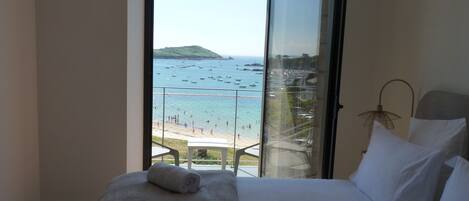 A bedroom with a large window overlooking a beach and boats.