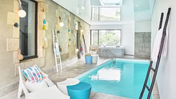 Relax by the pool surrounded by a glass ceiling and stone walls, with lounge chairs and a hot tub nearby.