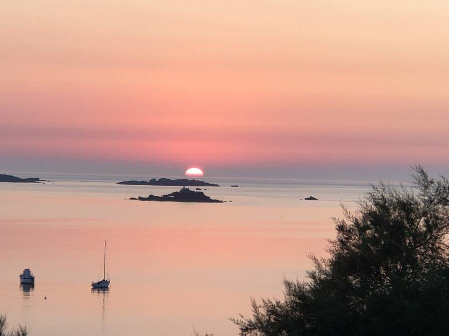 A calm sea with a sunset, boats, and distant islands.
