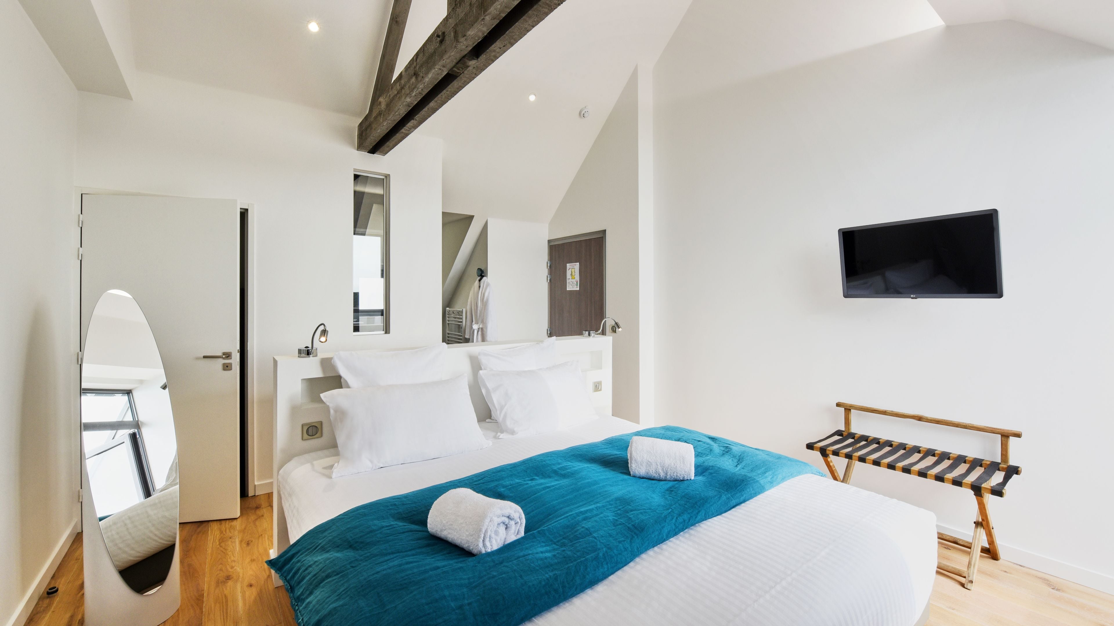 Un dormitorio moderno con una cama grande, un televisor en la pared y un banco de madera.