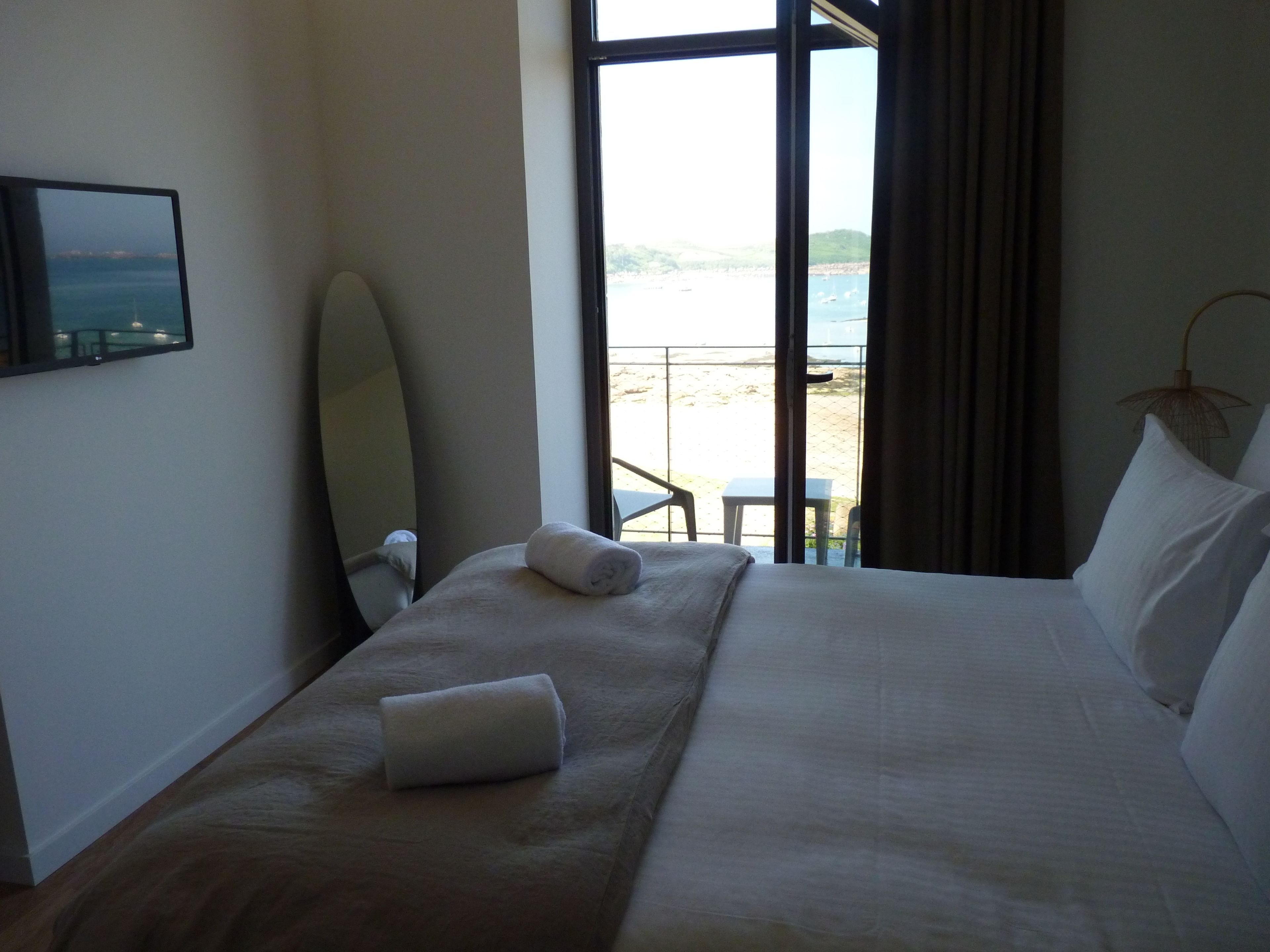 Ein Hotelzimmer mit Bett, Fenster mit Meerblick, einem Sessel und einem Tisch.