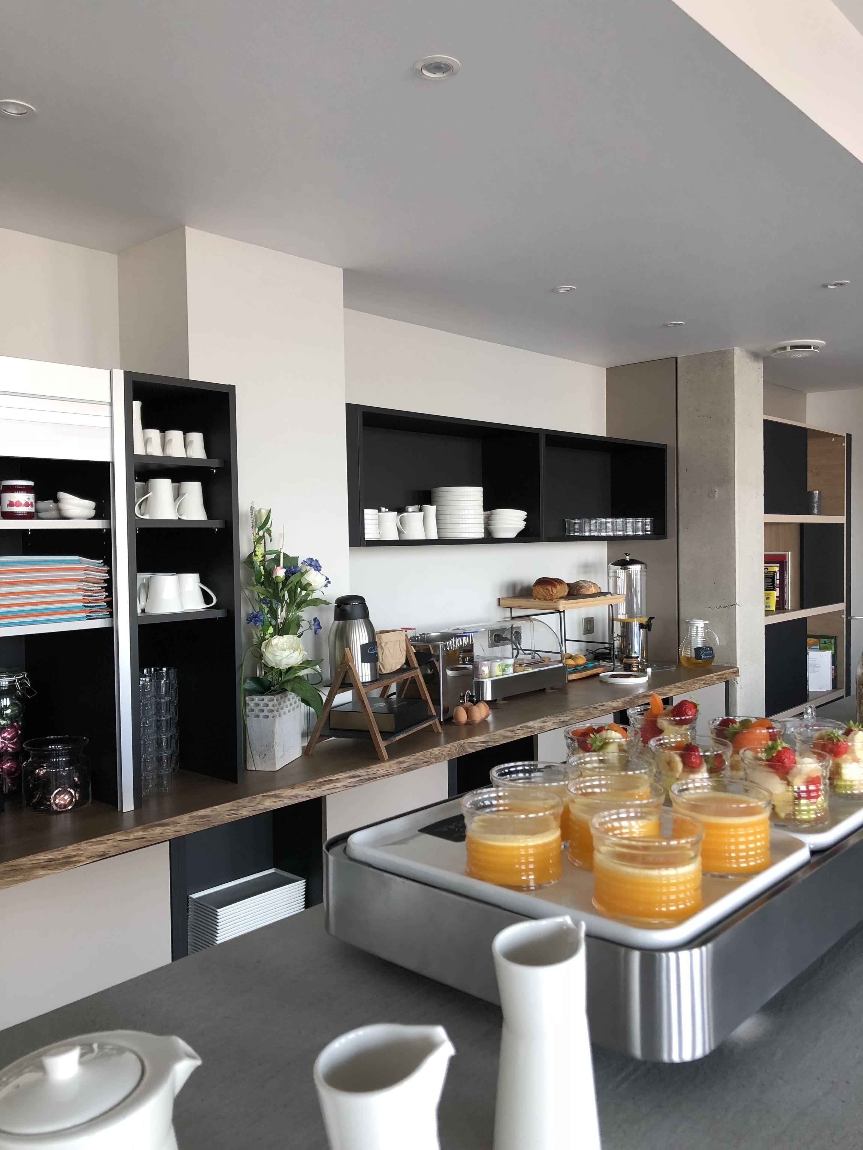 A modern kitchen with built-in appliances, a coffee station, and a buffet area with fruit and juice.