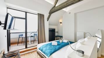 Una habitación de hotel moderna con una cama grande, un escritorio y un balcón con mesa y sillas.