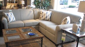 A living room with a sectional sofa, a glass-top coffee table, and a side table with a vase. - Metro Inn (Ranchi)