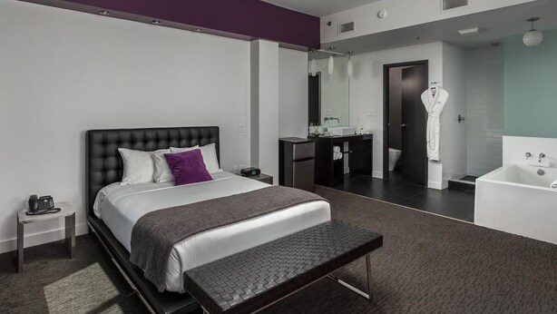 A modern hotel room with a large bed, a bench, a vanity with a mirror, and a separate bathroom with a bathtub. - Metro Inn (Ranchi)