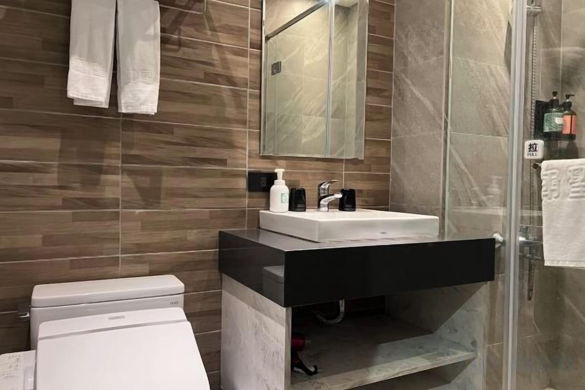 A modern bathroom with a white toilet, a black sink, and a glass shower enclosure.