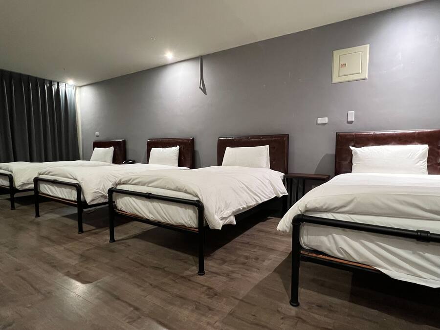 Habitación de hotel con cuatro camas individuales, cabeceros de madera y una pared gris oscuro.